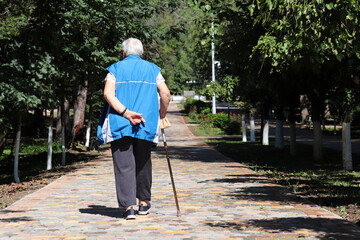 Old woman walking with a cane on a street in town park. Limping person, diseases of the spine, elderly people