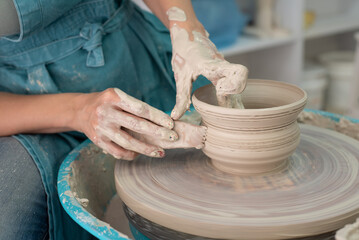 Person works on potter's wheel. Hands of potter sculpt pot from white clay. Workshop for manufacturing potter's products. Side view. Concept of creative, skill and handmade.