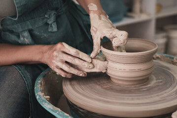 Person works on potter's wheel. Hands of potter sculpt pot from white clay. Workshop for manufacturing potter's products. Side view. Concept of creative, skill and handmade.