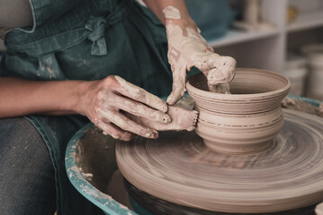 Person works on potter's wheel. Hands of potter sculpt pot from white clay. Workshop for manufacturing potter's products. Side view. Concept of creative, skill and handmade.