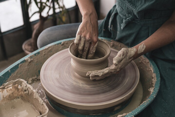Person works on potter's wheel. Hands of potter sculpt pot from white clay. Workshop for manufacturing potter's products. Top view. Concept of creative, skill and handmade.