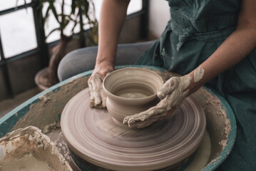 Person works on potter's wheel. Hands of potter sculpt pot from white clay. Workshop for manufacturing potter's products. Top view. Concept of creative, skill and handmade.