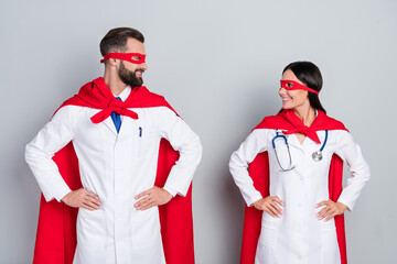 Portrait of two attractive cheerful therapists medics leaders team hands on hips isolated over grey...