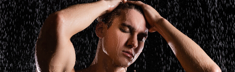 man with hands on head showering with closed eyes on black background, banner.