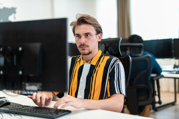 Fototapeta premium Casual man working on desktop computer in modern open plan startup office interior. Selective focus 