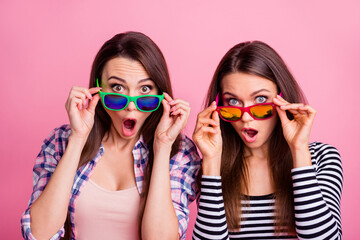 Portrait of two impressed pretty girls hands touch glasses open mouth isolated on pink color...