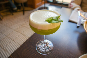 Green alcoholic drink with white foam with green basil leaf in a glass, soft drink, cocktail in a bar, restaurant, cafe. Frozen mint creme cocktail in menu. Beverage liquor with lime, rum and sugar.