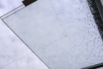 Raindrops on a transparent glass roof under a cloudy spring sky and lines of wires, urban minimalism