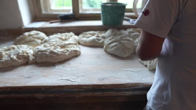 Baker kneading dough for bread on table.