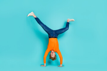 Full length photo of funky funny guy dressed orange sweater dancing walking arms isolated turquoise...