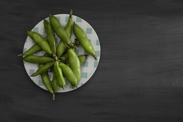 Round plate with shelled broad beans on a black wooden base and copy space