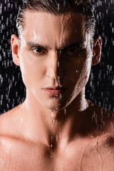 portrait of confident man looking at camera under raindrops on black background.