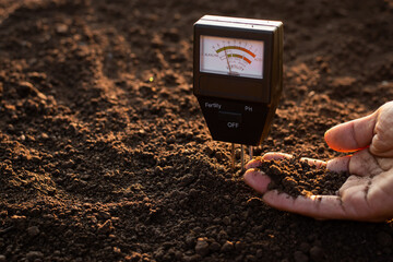 A soil meter and a farmer's hands are picking up soil for planting.