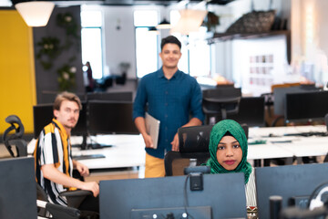 Fototapeta na wymiar Multiethnic startup business team Arabian woman wearing a hijab on meeting in modern open plan office interior brainstorming, working on laptop and desktop computer. Selective focus 