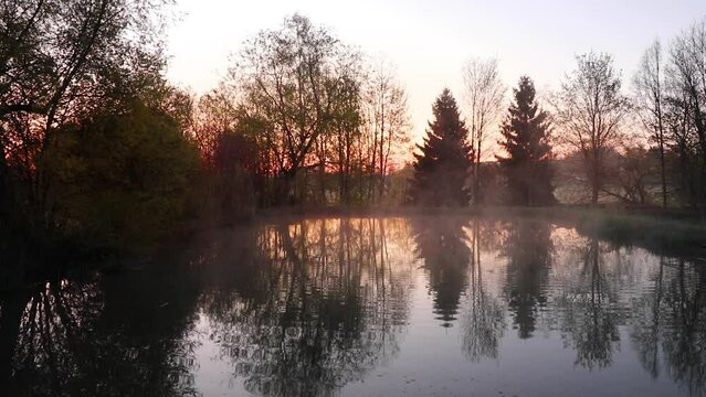 Tranquil morning at a pond in Bavaria at sunrise with mist rising from the water