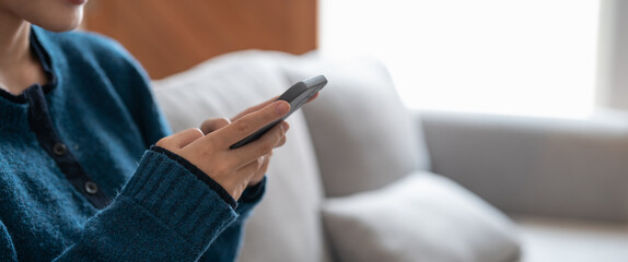 Close up of a woman using mobile smart phone on sofa at cozy home