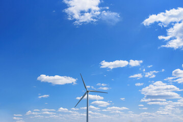 Wind turbine on blue sky with clouds.