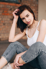 Fototapeta na wymiar Vertical photo of a portrait of a girl in jeans and a white t-shirt with short hair flowing stares into camera