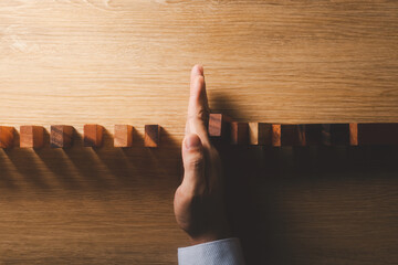 Risk management and business strategy concept, businessman hands stop the dominoes from falling continuously, preventing future risks from crisis.