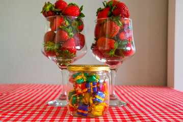 Fresh strawberries in glass wine glasses on a red and white tablecloth on the table.