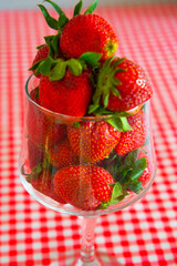 Fresh strawberries in a glass wine glass on red and white tablecloths on the table