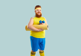 Portrait of happy overweight redhead man in sportswear isolated on blue studio background ready for...