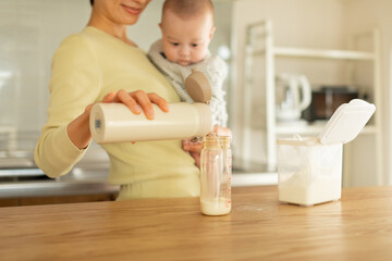 赤ちゃんを抱っこしながらミルクを作る母親