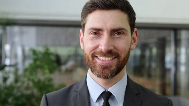 Close-up video portrait of a successful intelligent influential bearded caucasian businessman, corporate top manager or IT specialist, dressed in suit, looking at the camera, stand in modern office
