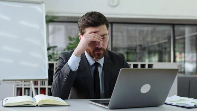 Tired caucasian intelligent businessman, company director, frustrated, didn't get a deal, failed project, tired of work with laptop, needs rest and break, gesturing hads,experiencing negative emotions