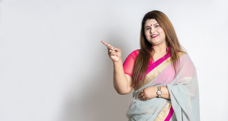 Happy Indian woman wearing saree shows blank space for your promotion isolated on white background, Overweight or plus size female model pointing finger for advertisement