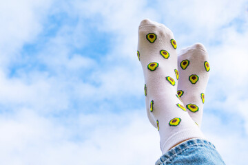 Legs in funny white socks with avocado on the background of clouds and sky.