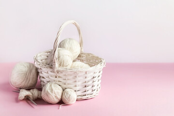 White balls of thread in a basket on a pink background for knitting warm clothes and hobbies needlework