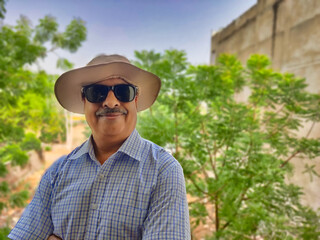 Picture of a person wearing sunglasses and hat out in a sanctuary in summers with green leaves in background