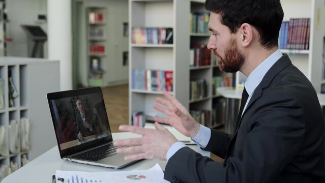 Two business colleagues are negotiating by video conference. Successful business man sits in a modern office, uses a laptop to communicate via video call with a business partner or client