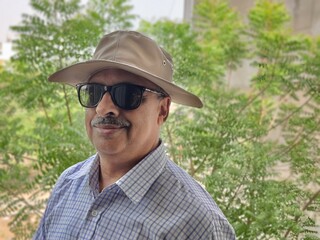 Picture of a person wearing sunglasses and hat out in a sanctuary in summers with green leaves in background