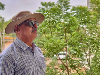 Picture of a person wearing sunglasses and hat out in a sanctuary in summers with green leaves in background