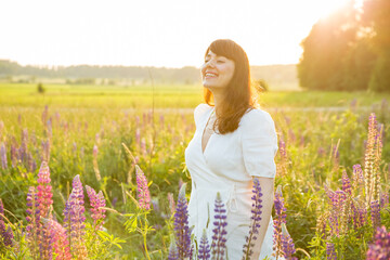 Beautiful woman in white sundress enjoying the summer nature. Picking flowers, breathing fresh air...