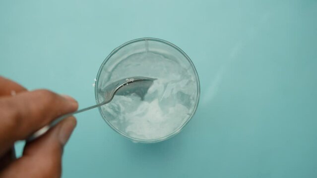 pouring white sugar in a glass of water on table 