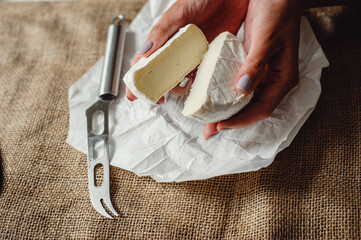 Cut Camembert cheese, French soft cheese with white mold in the hands of a woman on the background...