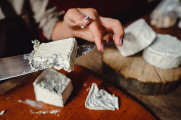 A piece of Valencay cheese on a knife. Cut the cheese with blue mold, close-up. Cheesemaker cuts french soft cheese with blue mold, closeup.