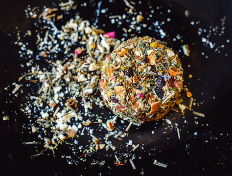 The round head of the French spicy cheese Boulette d'Avesnes sprinkled with different herbs, lies on a black plate. Close-up. Brin d'Amour