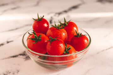 Tomates cherry orgánicos para ensalada, en un recipiente de vidrio sobre una  mesada de mármol con luz de día. Concepto de alimentación saludable.