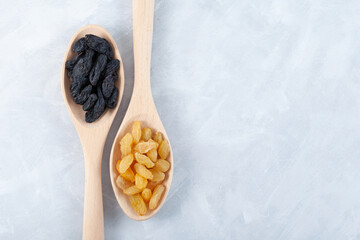 Black and Yellow raisins in wooden spoons on grey textured background, top view. Dried dehydrated grapes fruit. Selective focus, copy space