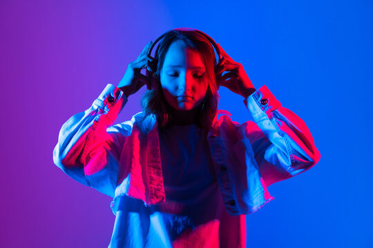 Hipster teenager beautiful fashion girl model wear stylish headphones enjoy listening to new cool music mix stand on purple studio background in trendy 80s 90s club blue party lighten background