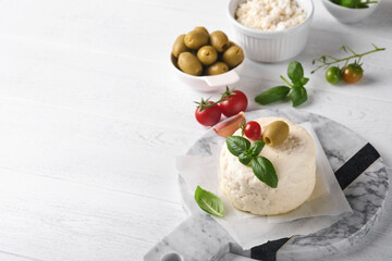 Ricotta cheese. Homemade Ricotta cheese with basil, garlic, tomatoes and green olives on parchment paperback and stand on old beige tiles background. Italian food. Selective focus.
