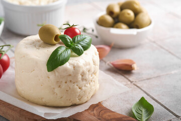 Ricotta cheese. Homemade Ricotta cheese with basil, garlic, tomatoes and green olives on parchment paperback and stand on old beige tiles background. Italian food. Selective focus.