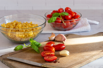 Tomates cherry orgánicos acompañados de ajo, aceite de oliva y pasta seca , sobre una mesada de mármol con luz de día. Concepto de alimentación saludable.