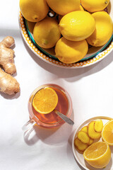 Big plate with lemons and a mug of tea and a ginger root and little plate of honey with a wooden spoon on a table covered with a white tablecloth. Folk way of treating colds