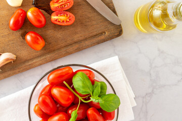 Tomates cherry orgánicos acompañados de ajo, aceite de oliva y pasta seca , sobre una mesada de mármol con luz de día. Concepto de alimentación saludable.