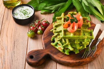 Green Belgian waffles. Spinach or wild garlic or pesto waffles with red salmon and cream sauce on black plate over dark rustic wooden background. Delicious breakfast, snack, brunch. Mock up